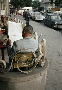 849492 Afbeelding van een man die de krant leest op het terras van het Centraal Station op het Stationsplein te Utrecht.